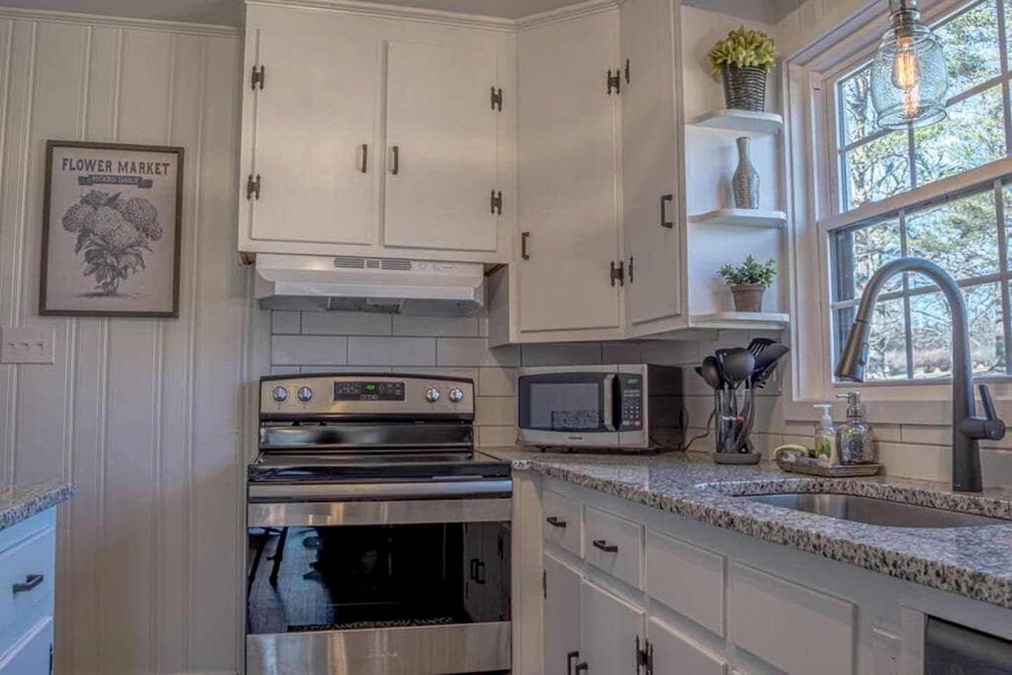 A kitchen with white cabinets, a stainless steel oven, a microwave, and a window with a view.