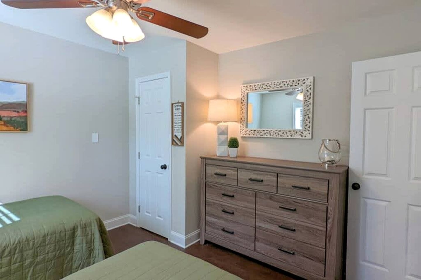 A bedroom with a bed, a dresser, a ceiling fan, a door, and a wall-mounted mirror.