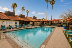 Ein Swimmingpool mit Liegestühlen, Palmen und einem Gebäude mit einem Ziegeldach.