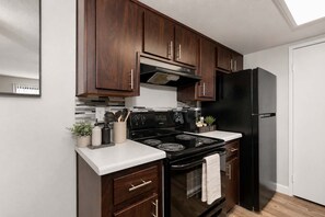 A kitchen with dark wooden cabinets, a black refrigerator, and a stainless steel stove. - Stylish 2BR in Tempe | Near ASU w/ Pools & Gym (Tempe)
