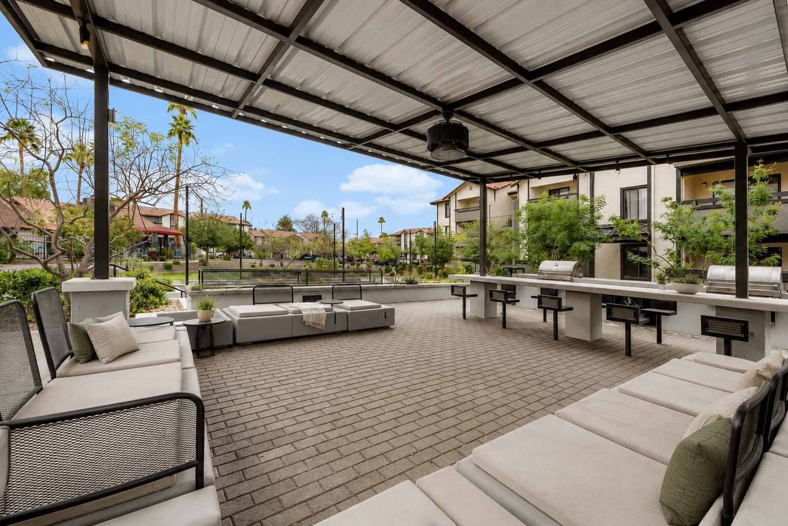 An outdoor patio with a covered seating area, a grill, and potted plants.