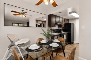 A modern kitchen with dark cabinets, a black refrigerator, and a dining area with a glass table and chairs. - Stylish Suites: Pet-Friendly 2BR in Tempe | Near ASU w/ Pools & Gym (Tempe)