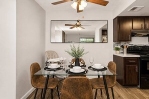 A dining area with a glass table, four chairs, a ceiling fan, and a kitchen in the background. - Stylish 2BR in Tempe | Near ASU w/ Pools & Gym (Tempe)