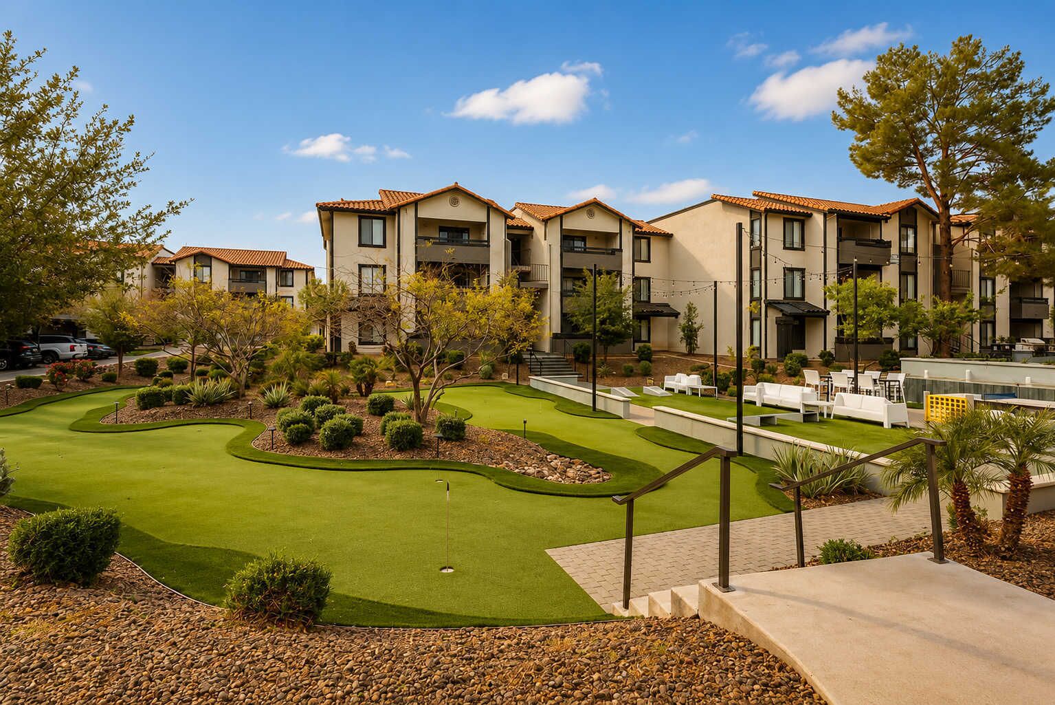 A golf course with a putting green, surrounded by a landscaped area with trees and shrubs, and a building with multiple balconies in the background.