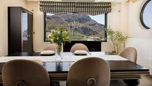 Ein Essbereich mit einem Tisch für vier Personen, ein Fenster mit Blick auf eine Berglandschaft und ein Ausblick zum Himmel durch das Fenster.