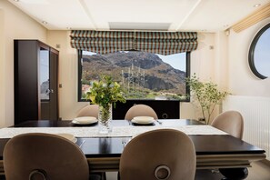 Ein Essbereich mit einem Tisch für vier Personen, ein Fenster mit Blick auf eine Berglandschaft und ein Ausblick zum Himmel durch das Fenster.