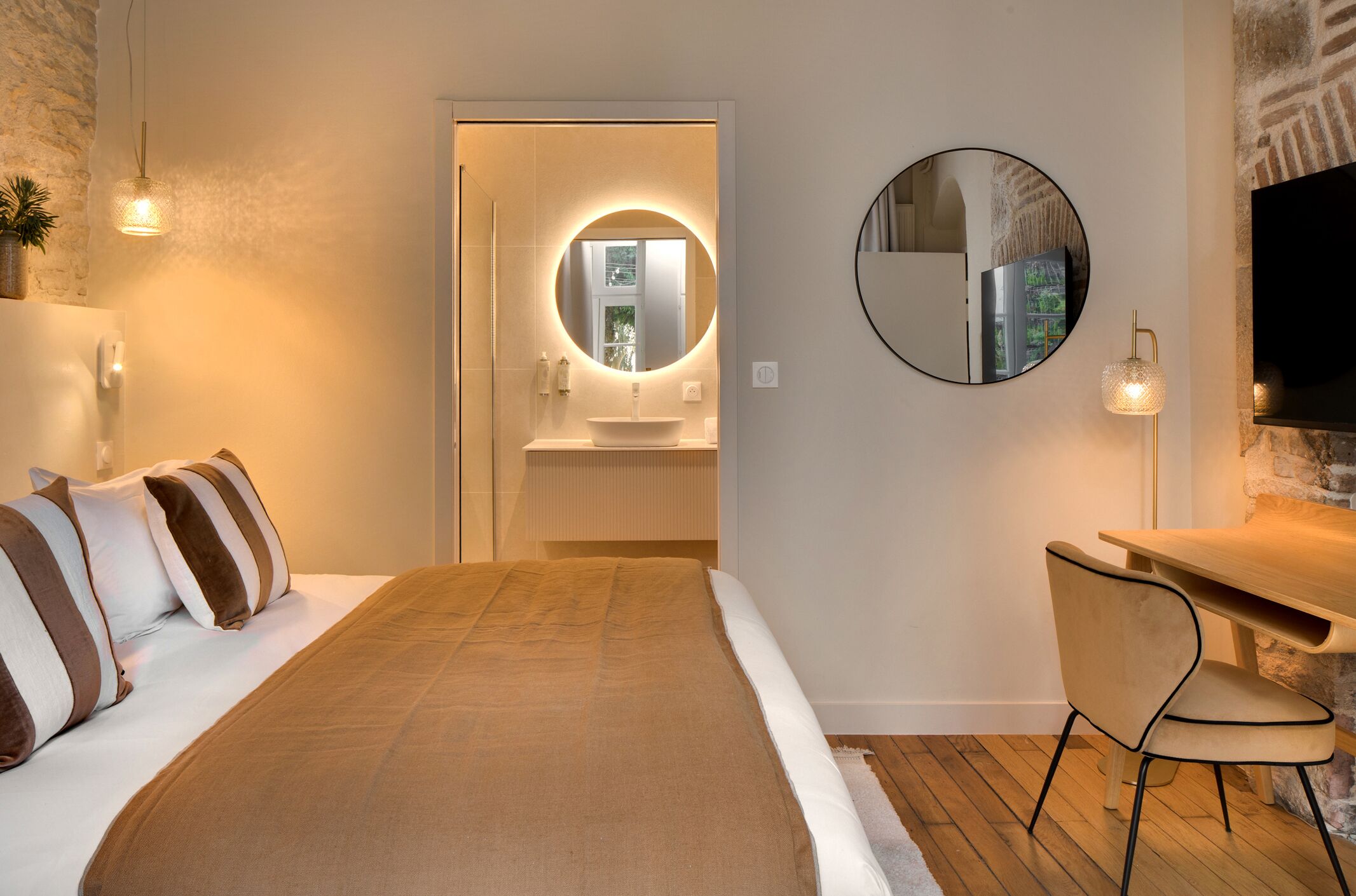 A hotel room with a bed, a desk, a round mirror, and a television.