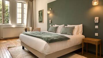 A bedroom with a bed, bedside tables, a radiator, a window with curtains, and a wall-mounted light fixture.