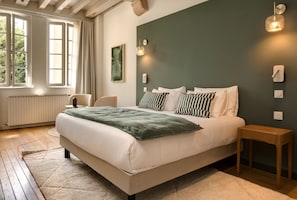 A bedroom with a bed, bedside tables, a radiator, a window with curtains, and a wall-mounted light fixture.
