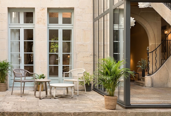 A building entrance with a staircase, a seating area with chairs and a table, and potted plants.