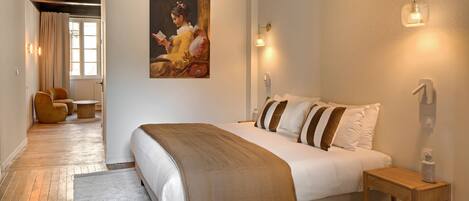 A bedroom with a large bed, a painting on the wall, and a view of the outdoors.