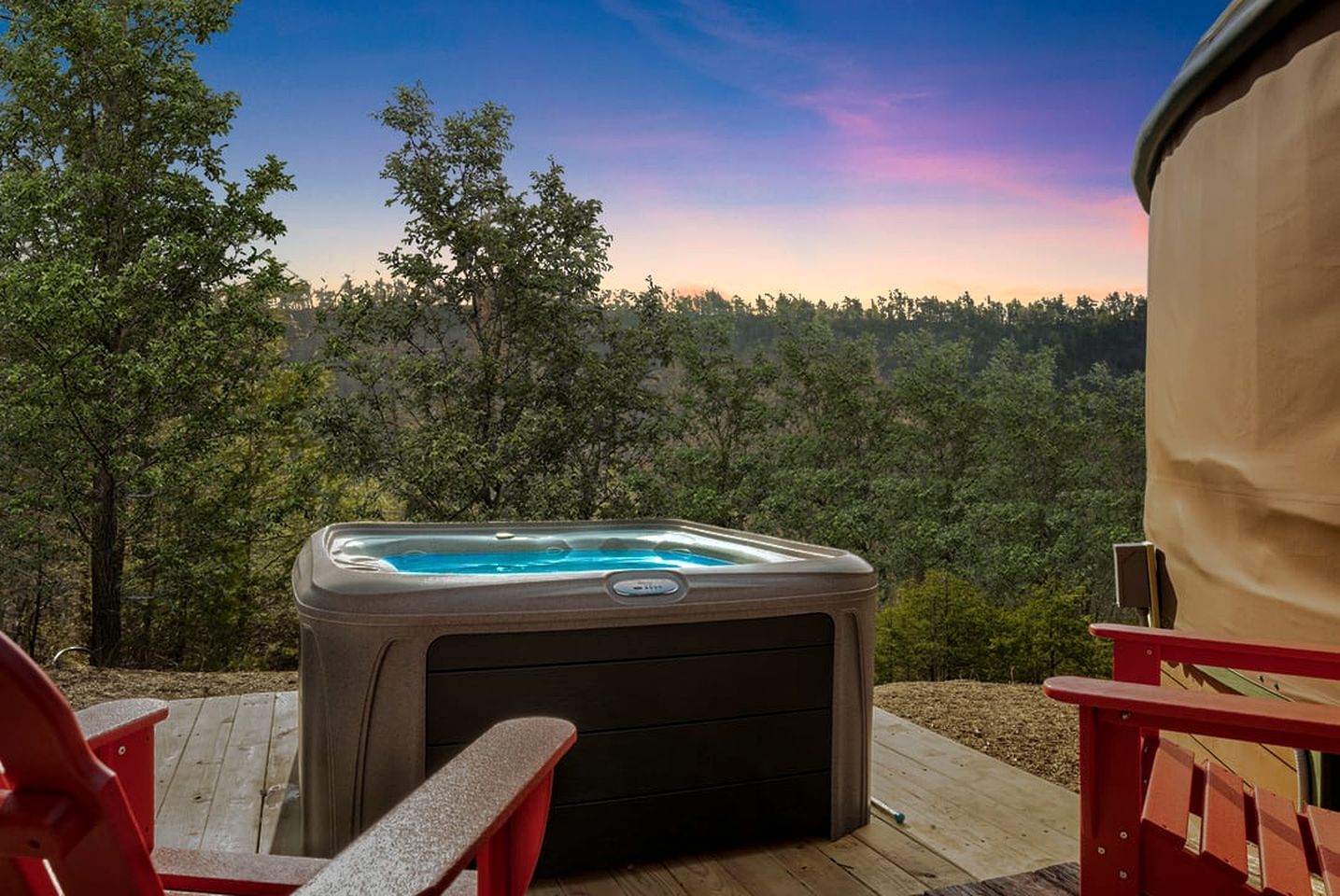 A hot tub on a wooden deck with a view of a forested area.