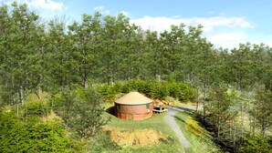 A yurt with a conical roof, surrounded by a forested area with a gravel path leading to it. - Fantastic Yurt with Hot-tub and Fire Pit in Wardensville, West Virginia (Wardensville)