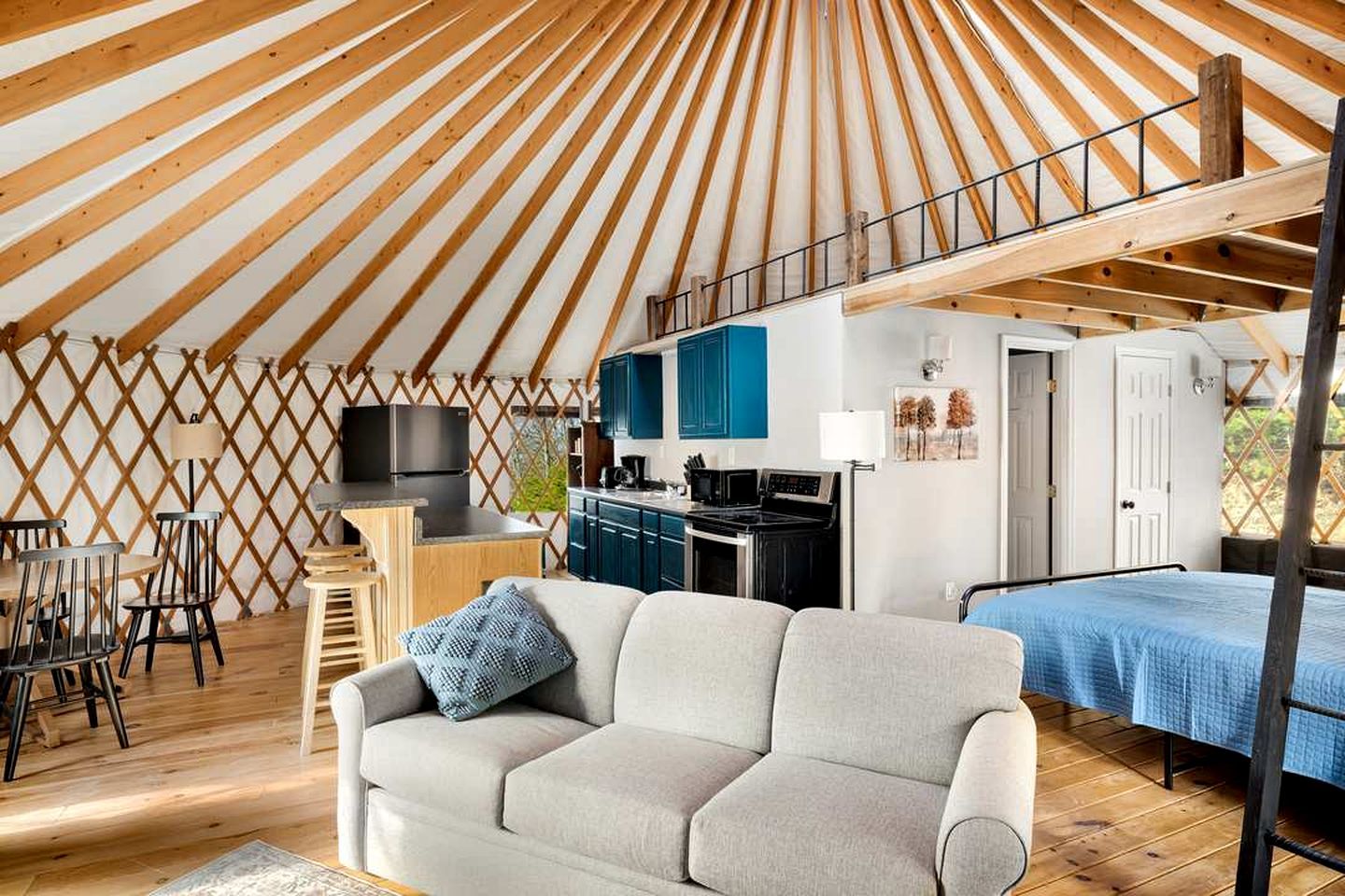 A yurt interior with a sofa, dining area, kitchen, and a bed.