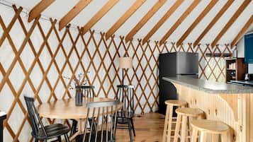 Een eetgedeelte met een houten tafel en stoelen, een bargedeelte en een keuken met een fornuis en kasten.
