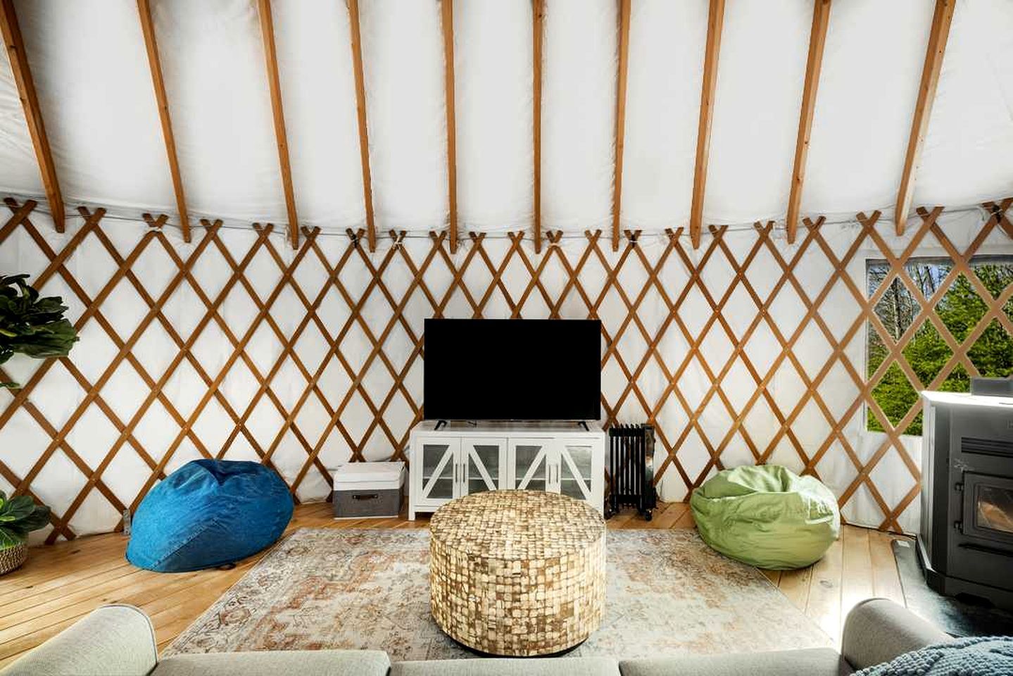 Een gezellige kamer met een televisie, een wit kastje, een geweven poef en een groene relaxstoel.