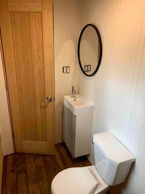 A small bathroom with a wooden door, a white sink, a toilet, and a mirror.