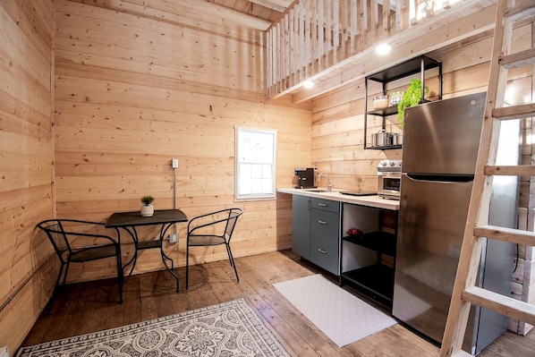 A compact kitchen with wooden walls, a dining area with a table and chairs, and a refrigerator.