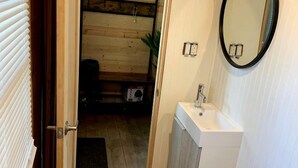 Ein schmaler Korridor mit Holzboden führt zu einem Badezimmer mit Waschbecken und rundem Spiegel.