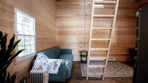Ein Holzblockhaus im Inneren mit einem blauen Sofa, einer Himmelsleiter, einer Heizung und einem Kühlschrank.