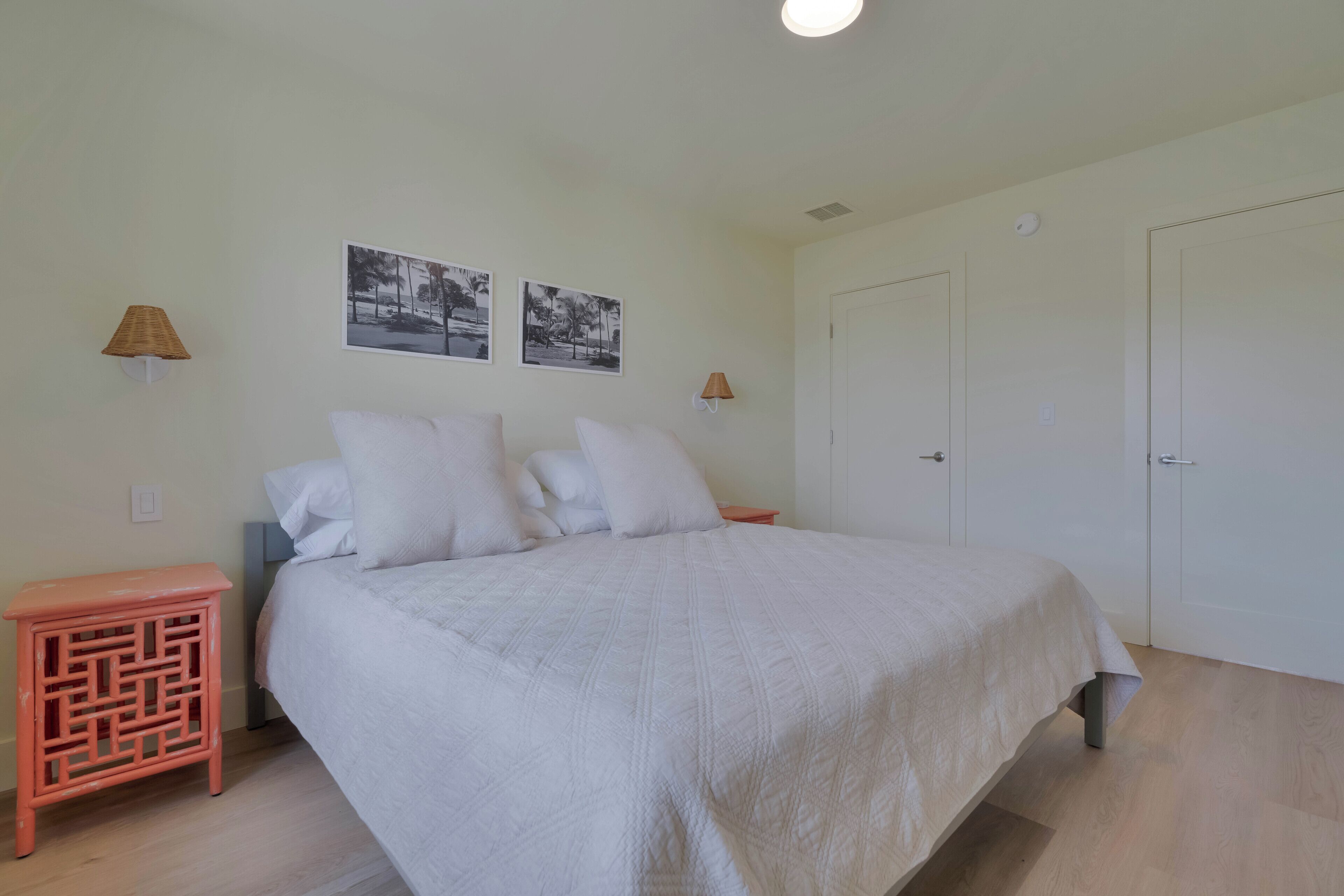 Un dormitorio con una cama, dos lámparas de pared, una puerta y dos cuadros en la pared.