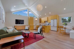 A modern kitchen with a large island, a dining area with chairs, a sofa, and a TV in a living room. - Marigold House is a luxury 5-bedroom vacation rental in York, Maine, just 0.5 miles from Long Sands Beach, with brand-new high-end appliances, upscale finishes, and plenty of space for families and groups. (York)