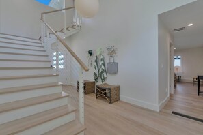 Ein modernes Interieur mit einer Holztreppe, einer an der Wand befestigten Pflanze und einer Sitzecke mit gemusterten Kissen.