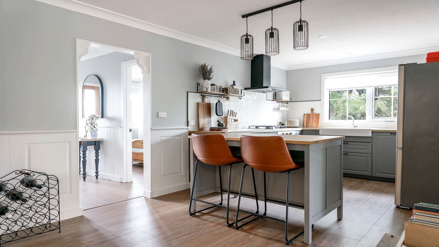 A modern kitchen with a central island, bar stools, pendant lighting, and a view to the outside.