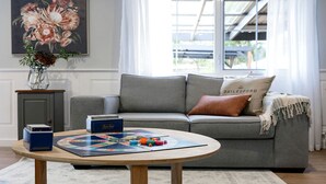 A living room with a grey sofa, a round wooden coffee table, and a board game. - Amazing Vacation Rental with Fireplace in Daylesford, Victoria (Daylesford)