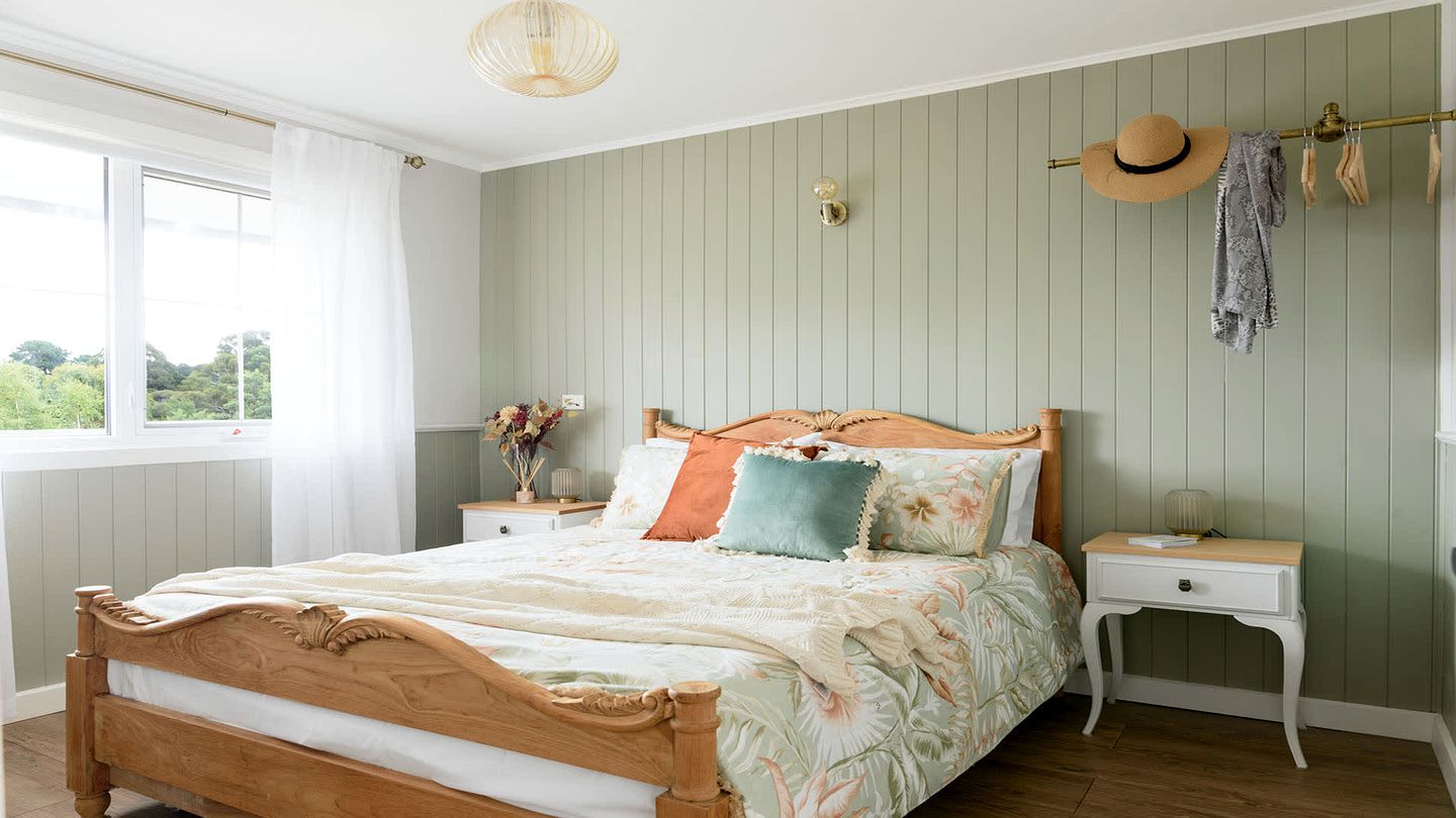 Een slaapkamer met een houten bed, een nachtkastje, een wandkapstok en een raam met gordijnen.