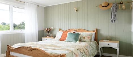 Une chambre à coucher avec un lit en bois, une table de chevet, un porte-chapeaux fixé au mur et une fenêtre avec des rideaux.
