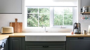 A kitchen with a white countertop, a wooden cutting board, a toaster, a kettle, and a window with a view of trees. - Amazing Vacation Rental with Fireplace in Daylesford, Victoria (Daylesford)