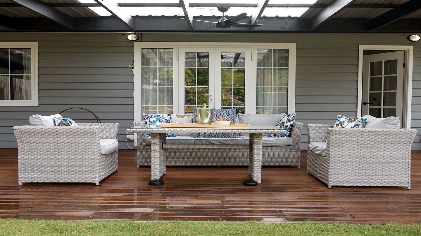 An outdoor patio with wicker furniture, a table, and a covered area with a ceiling fan.