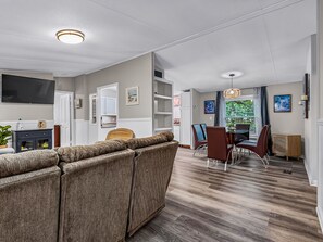 Un salon moderne avec un canapé d’angle, un coin repas avec des chaises et un téléviseur à écran plat fixé au mur.
