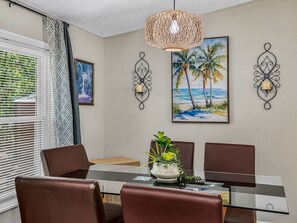 A dining area with a glass table, brown chairs, a woven pendant light, and wall-mounted sconces.