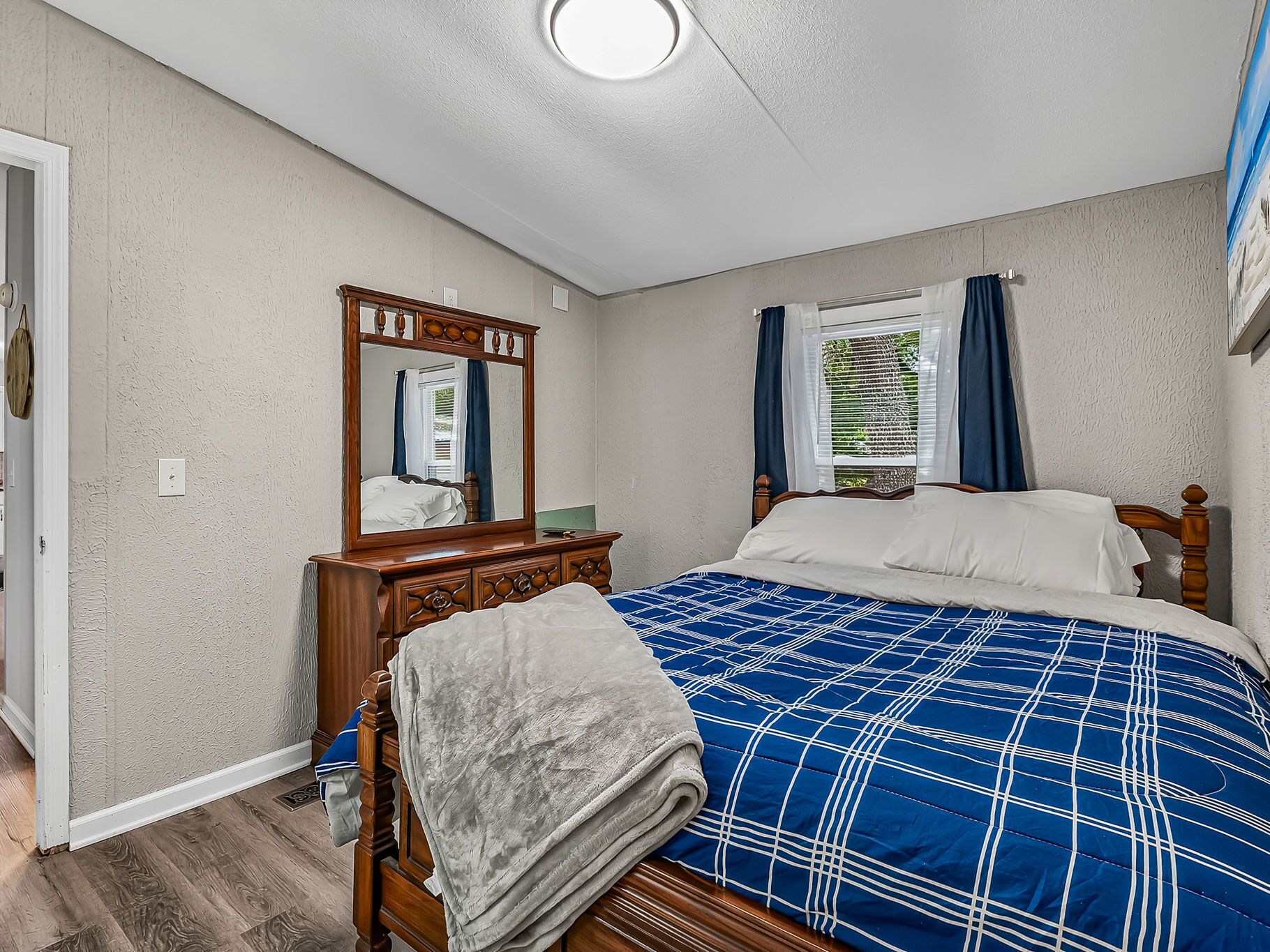 Un dormitorio con cama, cómoda, espejo y ventana con cortinas.