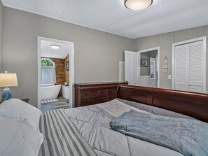 Ein Schlafzimmer mit Bett, Kommode, Nachttisch, Lampe und einem durchgegangenen Tür sichtbaren Badezimmer.
