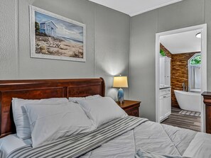Ein Hotelzimmer mit einem Bett, einem Nachttisch mit Lampe, einem Bild an der Wand und einem Badezimmer mit Badewanne und Dusche.