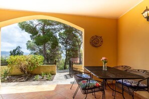 An outdoor patio with a table and chairs, a vase with flowers, and a view of trees and landscape. - Aetòs Home - Porto Pino (Porto Pino)