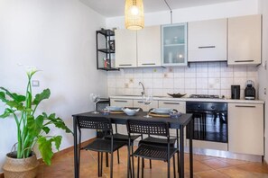 A modern kitchen with white cabinets, a black countertop, and a dining area with black chairs. - Aetòs Home - Porto Pino (Porto Pino)