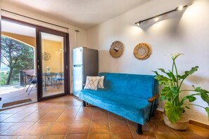 A room with a blue sofa, a refrigerator, a potted plant, and a dining table with chairs. - Aetòs Home - Porto Pino (Porto Pino)