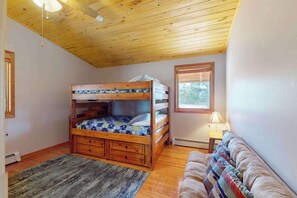 Ein Zimmer mit Etagenbett, einer Schlafcouch, einem Fenster und einem Deckenventilator.