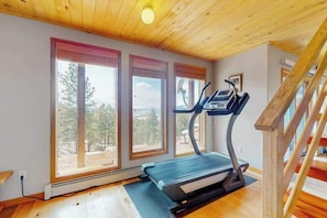 A room with a treadmill, large windows, and a wooden ceiling. - Hot Tub Mountain Home • Big Deck • Pine Views (Florissant)