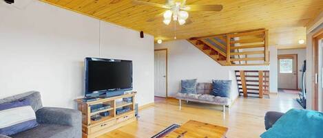 Un vaste salon doté d’un plafond en bois, d’un téléviseur à écran plat, d’un canapé, d’une table basse et d’un escalier menant à un autre niveau.