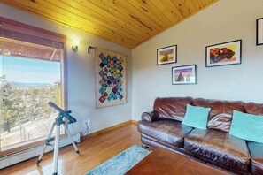 A room with a leather couch, a telescope, and artwork on the walls. - The Mountain Artist's Retreat - Secluded Mtn Home • Hot Tub & Big Deck (Florissant)