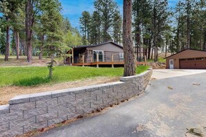 A cabin with a deck, surrounded by trees and a stone retaining wall. - Two Bit Cabin - Secluded Cabin • Hot Tub & ATV Trails (Deadwood)