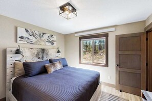 Um quarto com cama, penteadeira, janela com vista e porta.