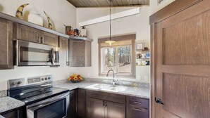 A modern kitchen with stainless steel appliances, dark wooden cabinets, a granite countertop, and a window providing natural light. - Rost Place Round-Up - Dog-Friendly Cabin • Mtn Views & BBQ (Sturgis)