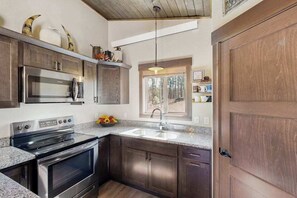 Uma cozinha moderna com eletrodomésticos de aço inoxidável, armários de madeira escura, bancada de granito e uma janela que oferece iluminação natural.