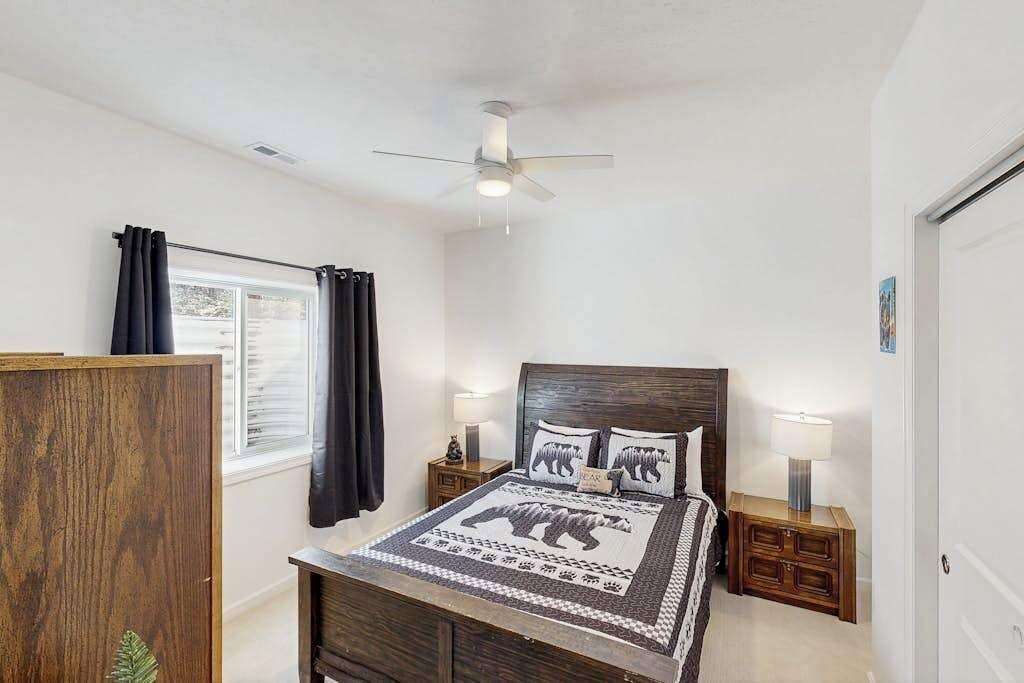 A bedroom with a bed, a ceiling fan, a window with curtains, and bedside tables with lamps.